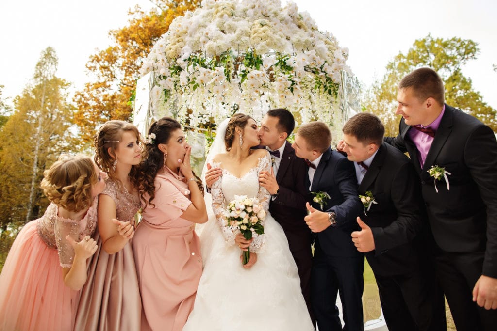 Wedding Party standing in front of floral arch wearing different outfits
