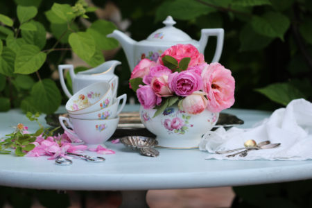 Tea party in garden: vintage china set floral pattern on metal tray, silver ton spoons, tea strainer on linen napkin, garden scissors, rose bowl with roses, outdoor and space, daylight, summertime